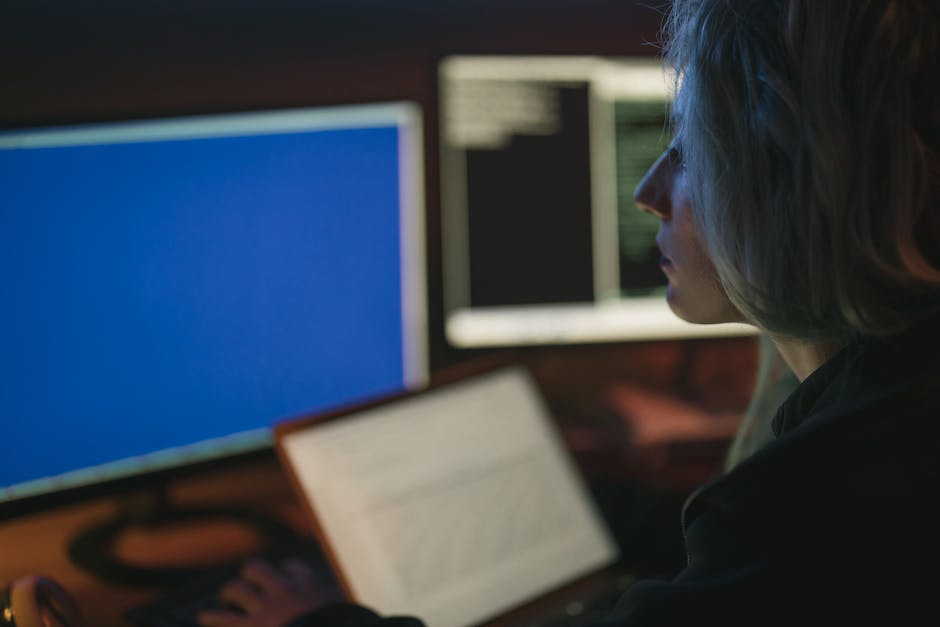 A woman working on multiple computer screens at night, focusing on her tasks.